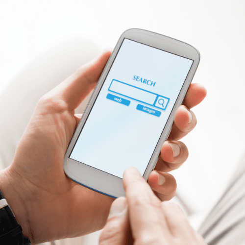 7 Person holding a smartphone with a search engine page open, finger touching the screen near the search bar.