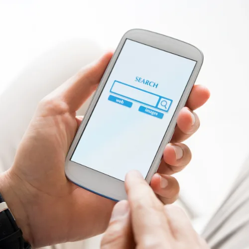 Person holding a smartphone and using a search engine to browse websites and social media options on screen.