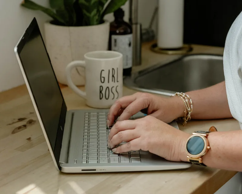 A person works on seo at a kitchen counter, Girl Boss mug beside their laptop.