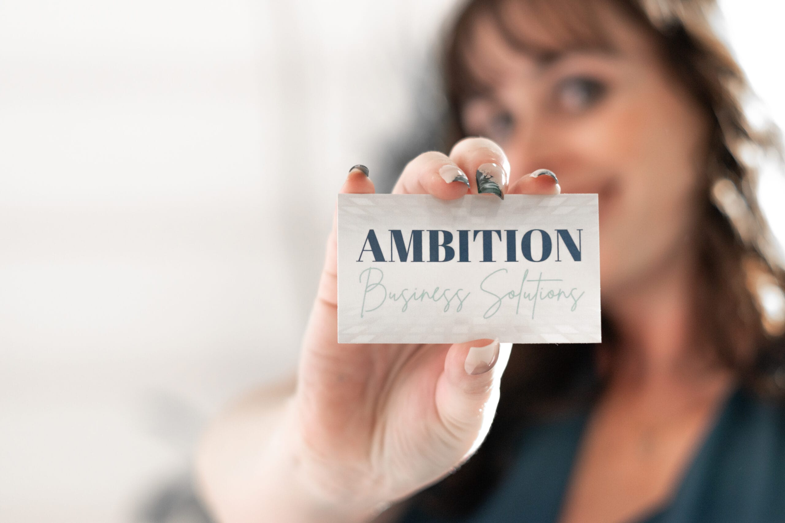A person holding a card that says AMBITION Business Solutions with a blurred background. A person holding a card that says AMBITION Business Solutions with a blurred background.