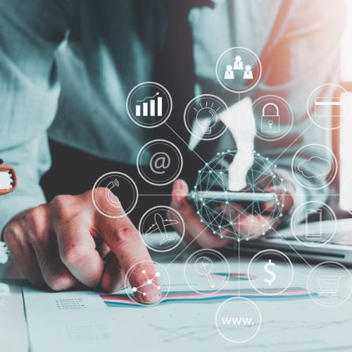 Businessperson using a smartphone with digital icons overlay, analyzing charts and graphs on a desk.
