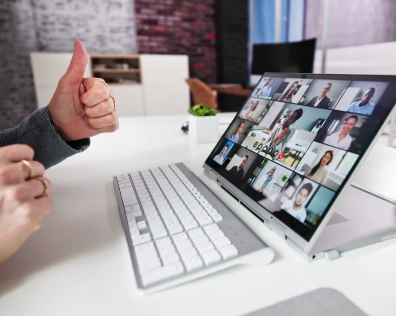 Person giving a thumbs-up in front of a laptop, sharing a website demo on a video conference with many participants.